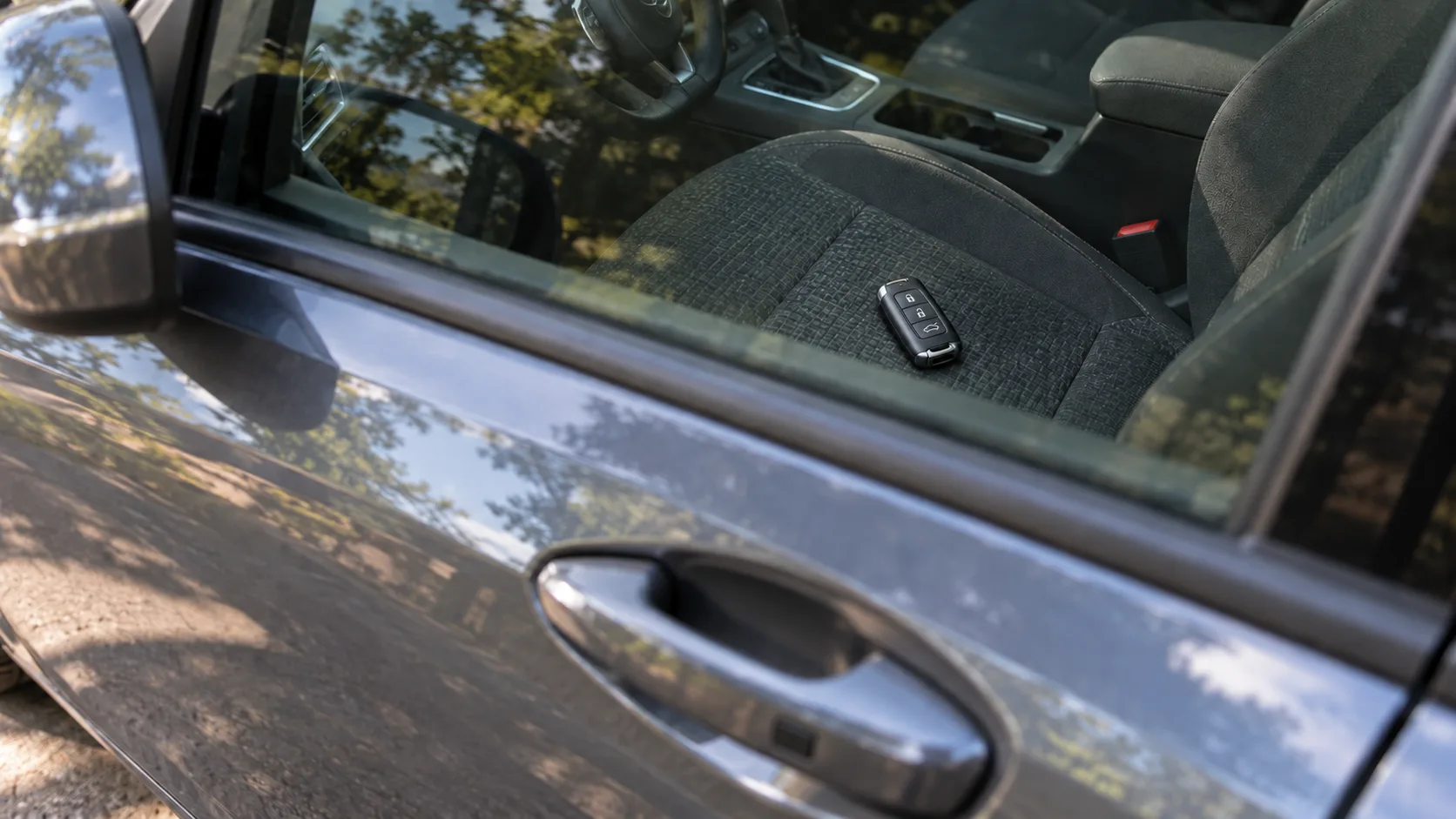 A key fob resting on the driver's seat of a car, seen through the closed window